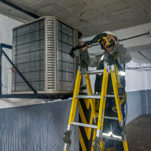 tecnico en escalera limpiando condensador imagen mejorada